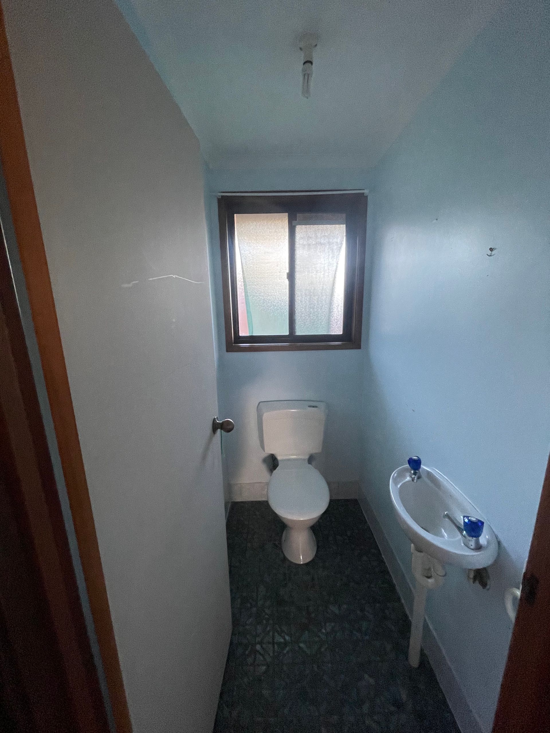 Small bathroom with a toilet, sink, and window; blue walls, dark floor — Smooth Flow Plumbing Cairns in Cairns City, QLD 