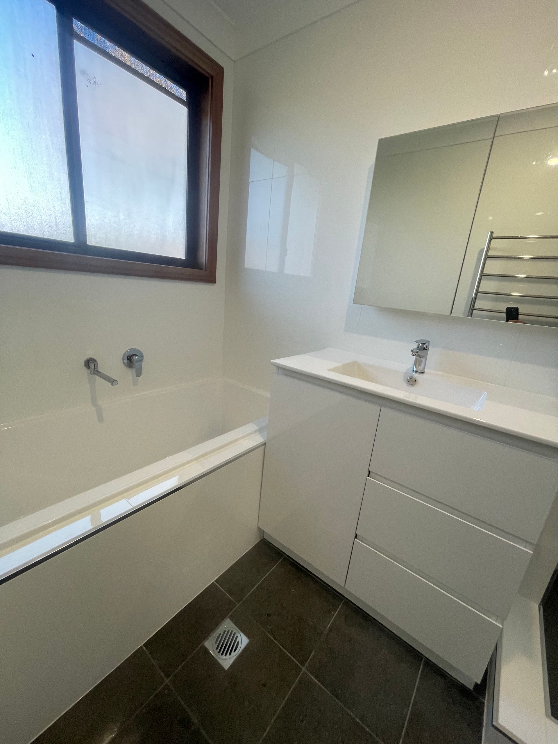 Bathroom with a white bathtub, vanity, and large mirror. Dark tile floor — Smooth Flow Plumbing Cairns in Cairns City, QLD 