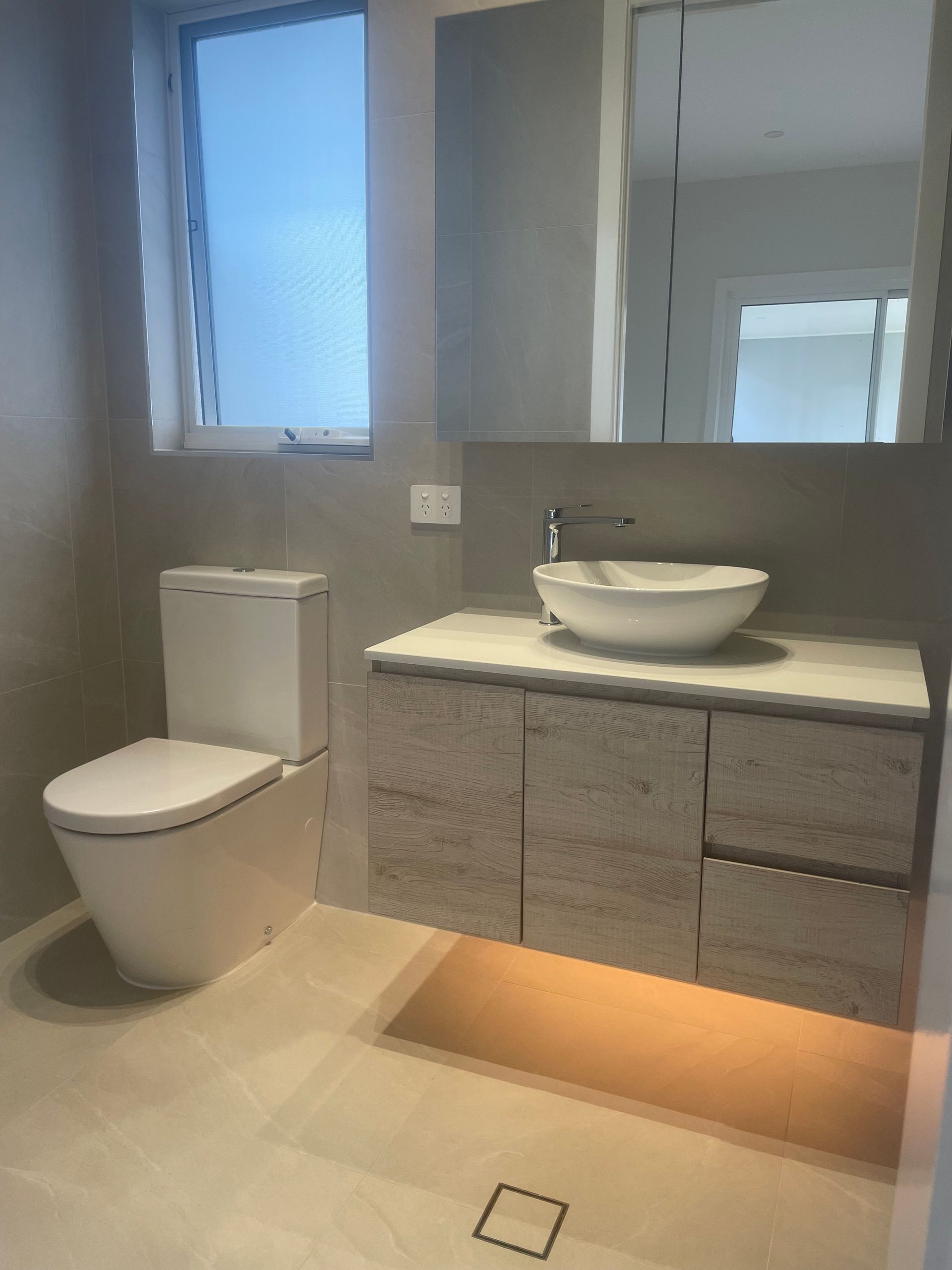 Modern bathroom with floating vanity, toilet, and window. Light gray and beige tones — Smooth Flow Plumbing Cairns in Cairns City, QLD 