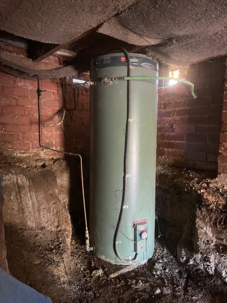 A green water heater in a dark, brick-walled basement — Smooth Flow Plumbing Cairns in Cairns City, QLD 