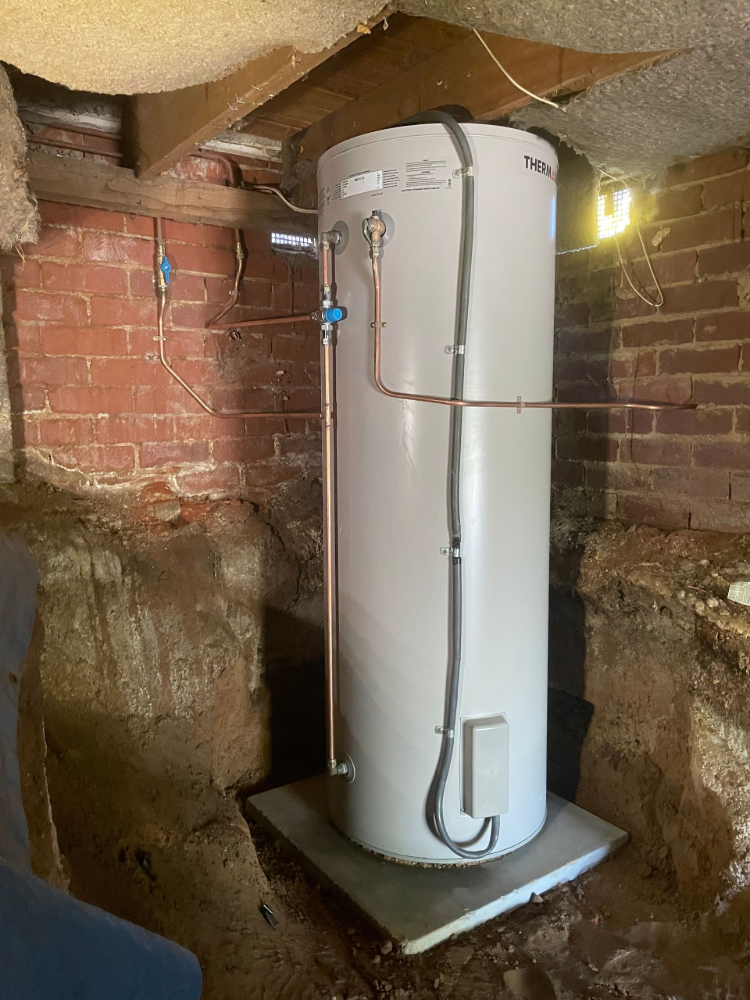 A tall, silver hot water heater in a brick-lined crawl space. Copper pipes are visible — Smooth Flow Plumbing Cairns in Cairns City, QLD 