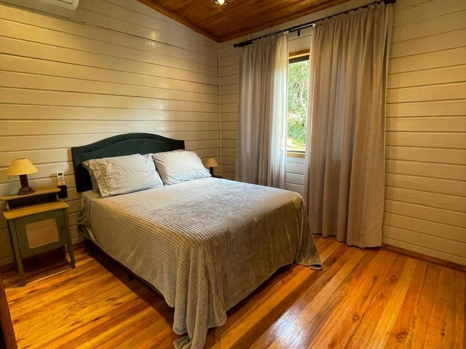 Quarto com cama, mesa de cabeceira, janela e paredes e piso de madeira.