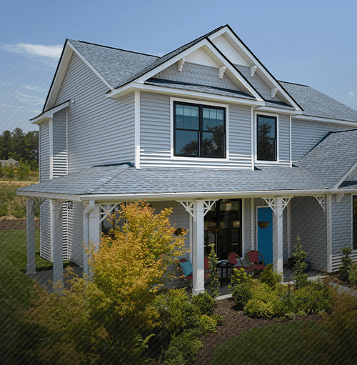 Two-story house with a blue front door and a wrap-around porch; surrounded by green landscaping.