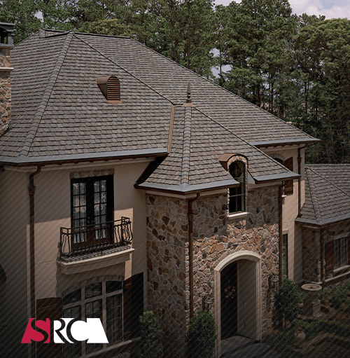 A stone-and-stucco house with a dark shingle roof.  It has a turret, dormer and black accents, with trees in the background.