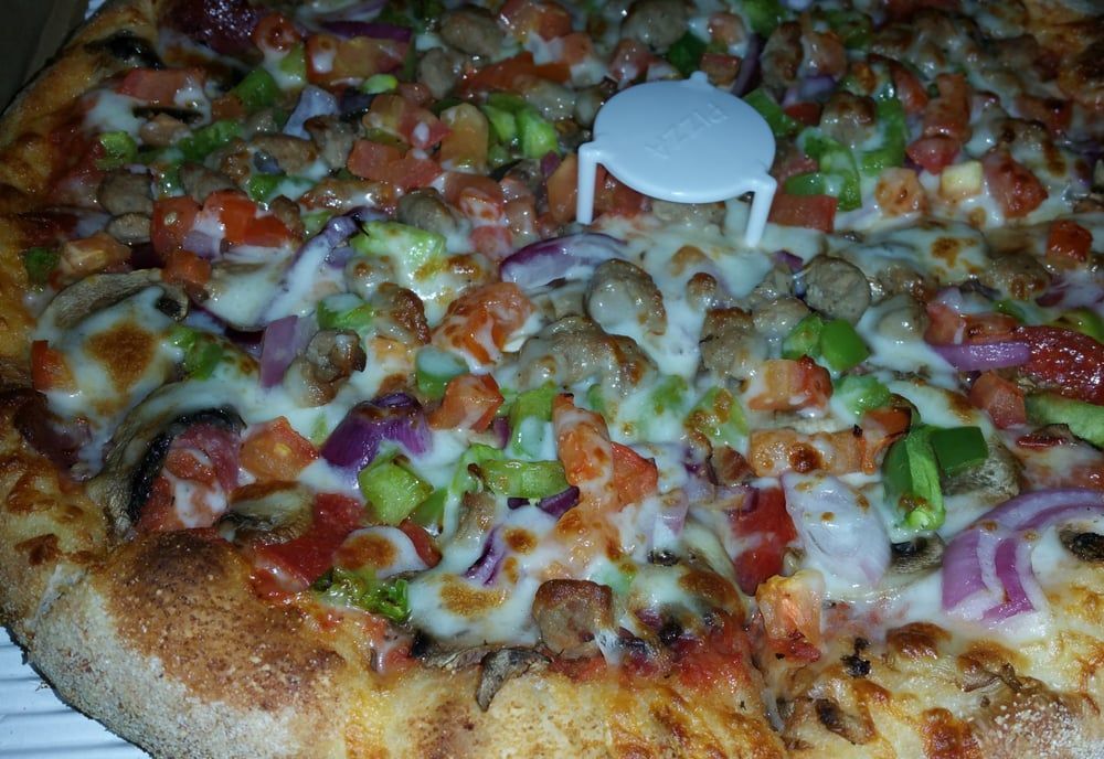 A pizza with lots of toppings and a pizza stand on top of it