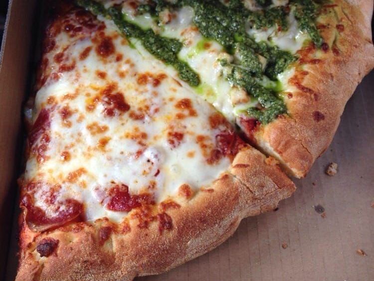 Pizza slice with red sauce and pepperoni, next to a slice with green pesto.