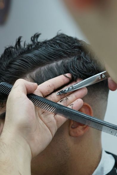 A man is getting his hair cut by a barber with scissors and a comb.
