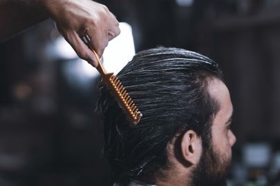 A man with a beard is getting his hair combed by a barber.