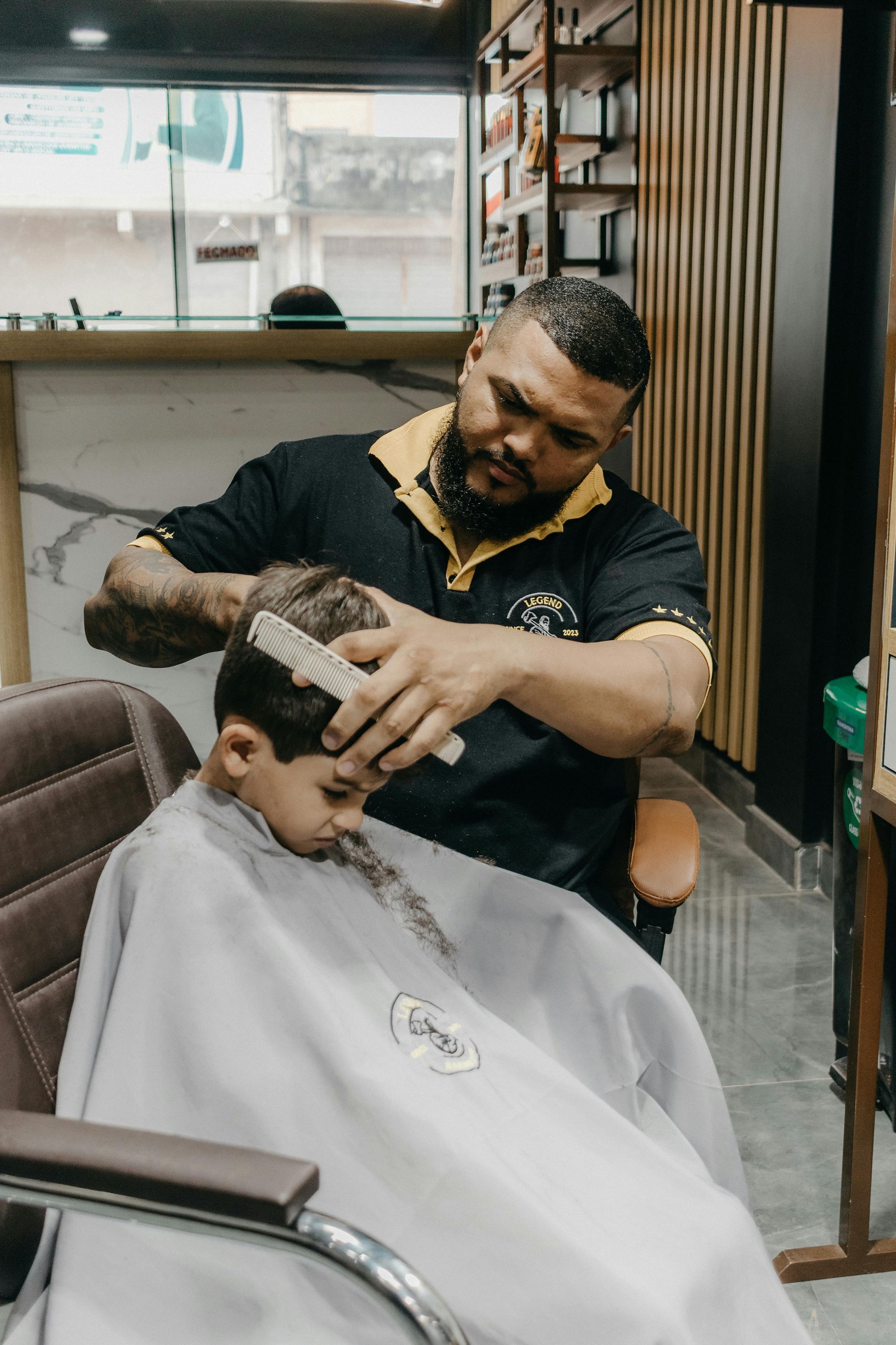 A young boy is getting his hair cut by a barber in a barber shop.