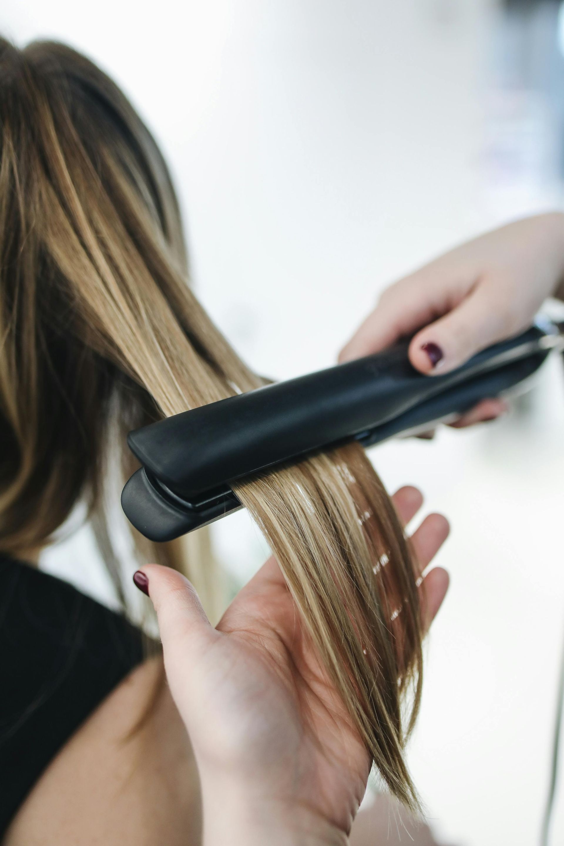 A woman is getting her hair straightened by a hairdresser.