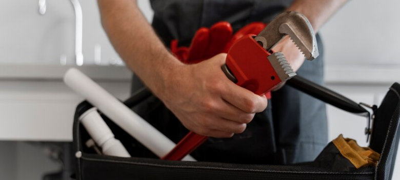 A plumber is holding a wrench in front of a toolbox filled with tools.