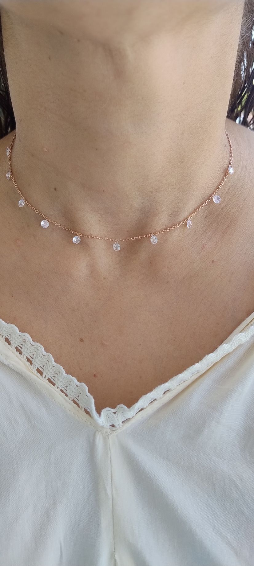 Primer plano de una persona que lleva un delicado collar de cuentas y una blusa blanca con ribete de encaje.