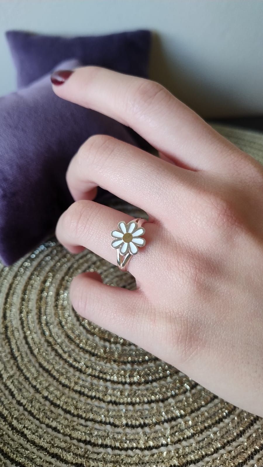 Una mujer lleva un anillo de plata con una margarita en el dedo.