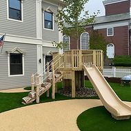 A wooden playground with a slide and stairs in front of a house.