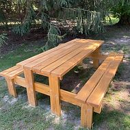 A wooden picnic table with two benches is sitting on top of a lush green field.