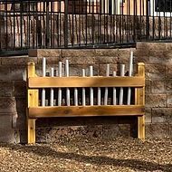 A wooden bench with pipes attached to it is sitting in front of a brick wall.