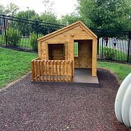 A small wooden playhouse with a porch in a park.