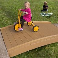 A little girl is riding a yellow tricycle on a wooden bridge.