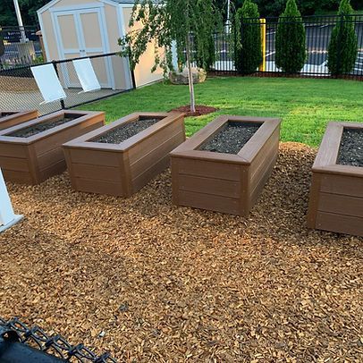 A row of wooden planters sitting on top of a pile of mulch in a yard.
