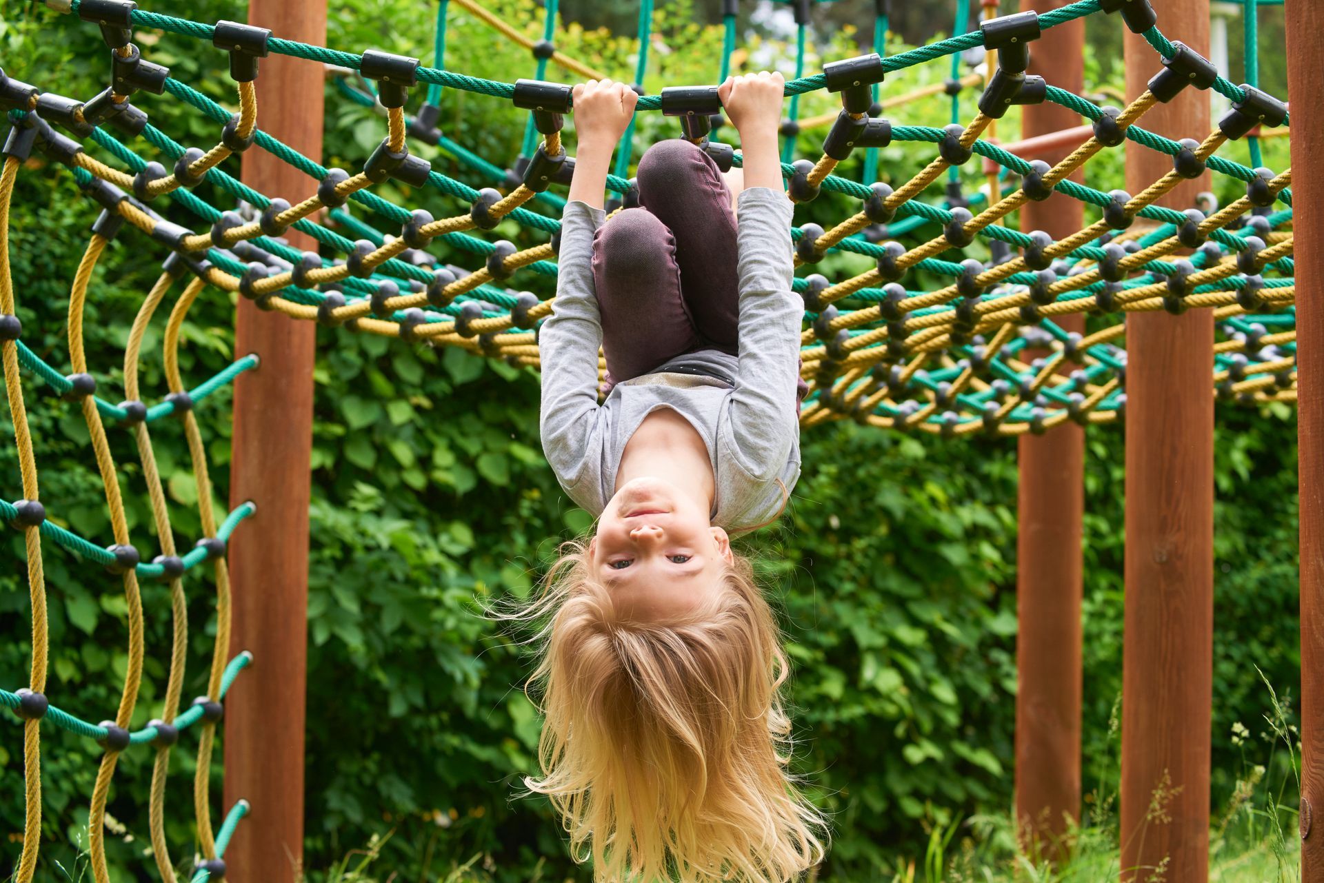 Child hanging upside down from a rope climbing net on a playground.
