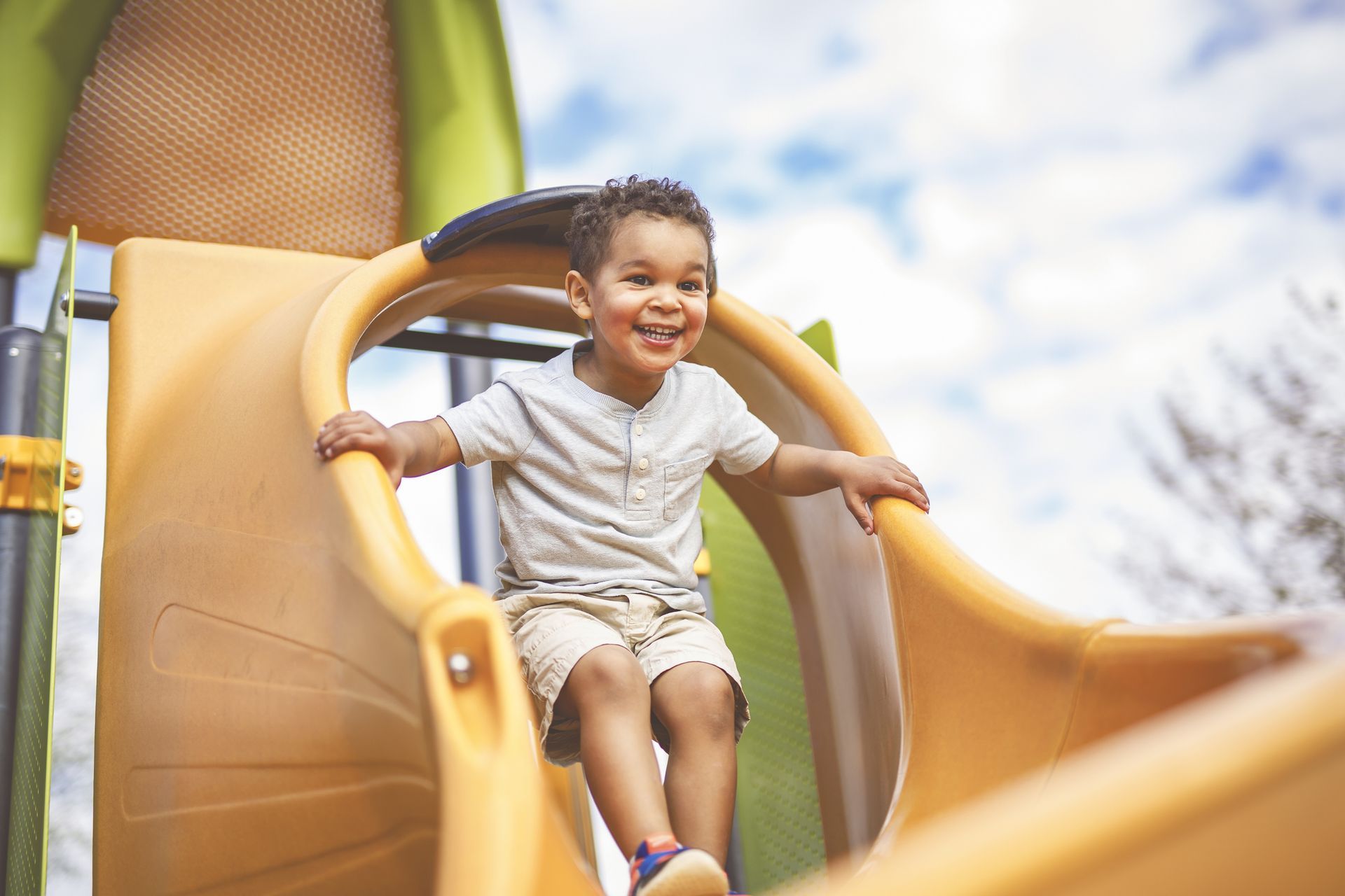 A child sits at the top of a yellow slide on a playground. A child sits at the top of a yellow slide on a playground.