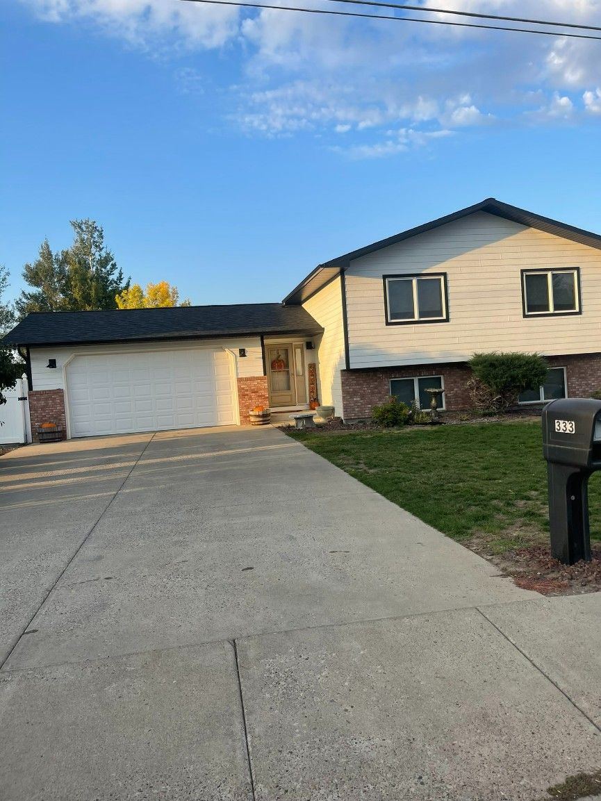 Two-story house with a white garage and driveway, brick accents, green lawn, and blue sky.
