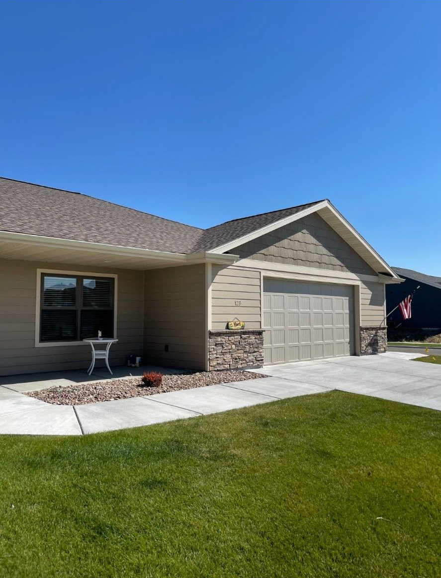 Tan house with a garage, stone accents, and a small garden, under a bright blue sky.