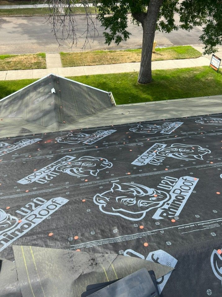 Black roofing underlayment with a rhino logo, roof in progress, residential area.