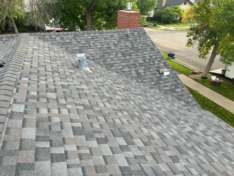 Gray asphalt shingle roof with a brick chimney and a small vent; trees and a street in the background.