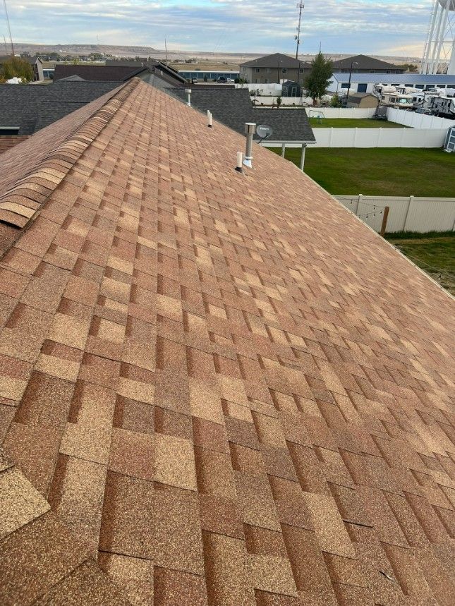 Brown shingle roof, angled view. Houses, sky, and some grass in background.