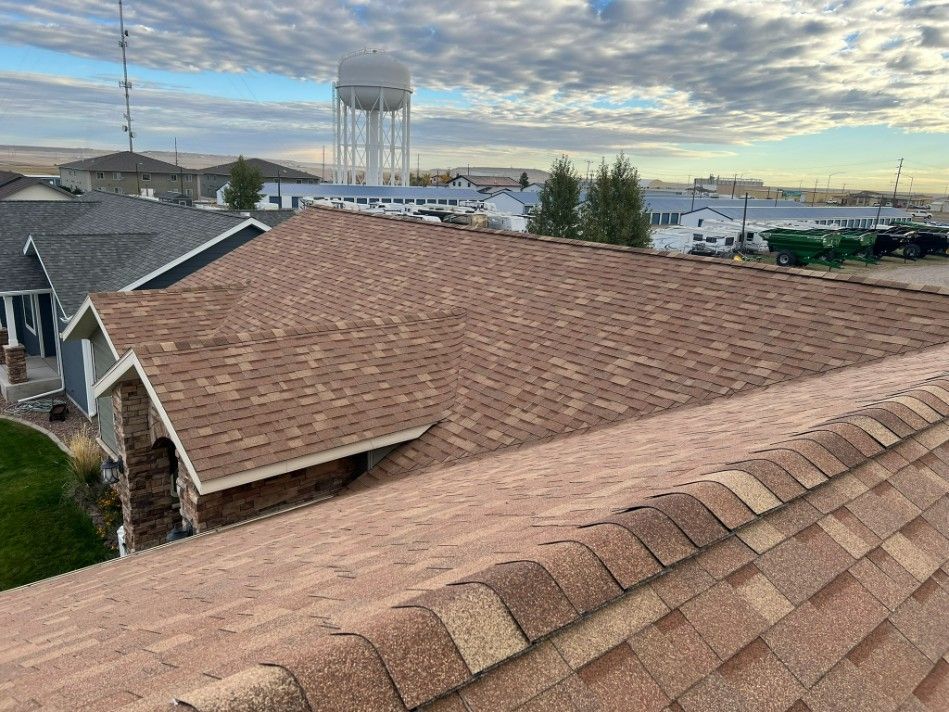 Brown shingle roof with a partial view of a town, water tower, and cloudy sky.