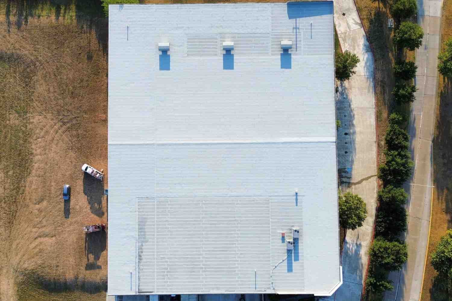 Aerial view of a large white commercial building with vents. Two vehicles and people are visible to the left.