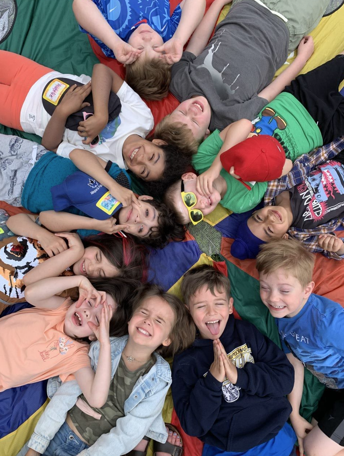 A group of children are laying in a circle on a parachute.