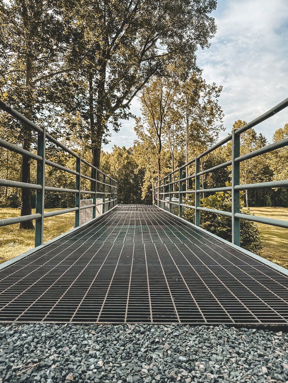 A bridge over a river in a park with trees in the background.