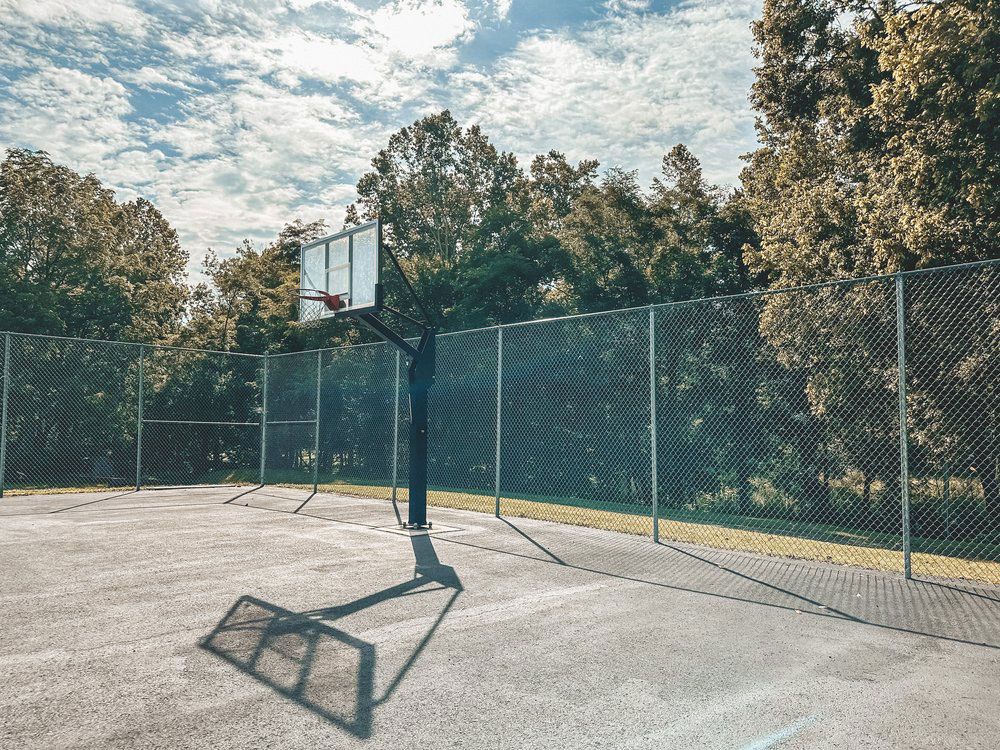 A basketball hoop is surrounded by a chain link fence in a park.