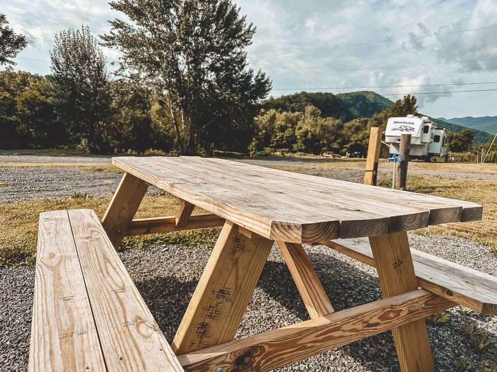 A wooden picnic table with benches in a field with mountains in the background.