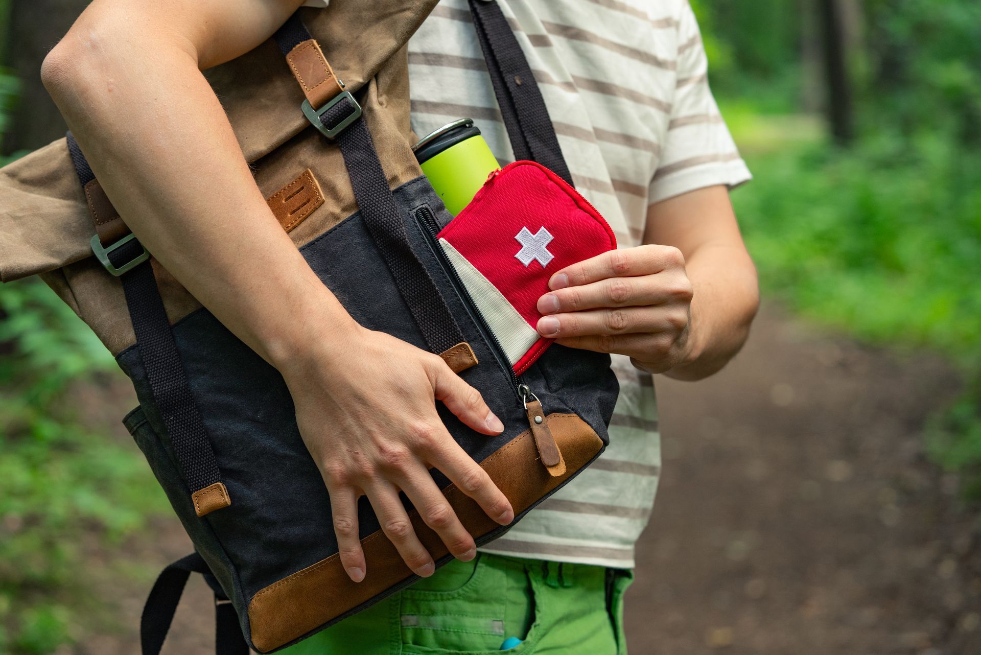 Person in forest, putting first aid kit into backpack.