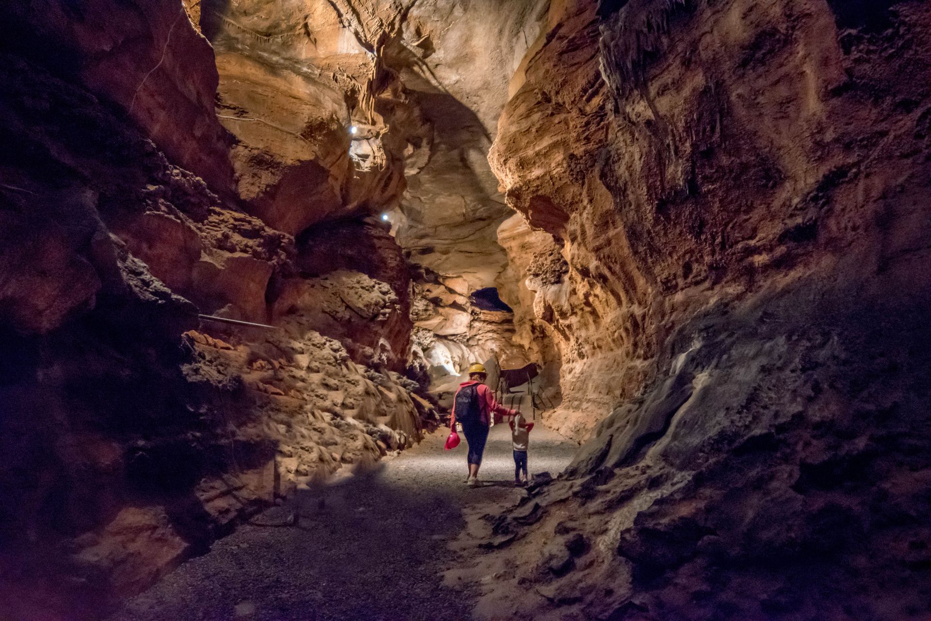People walking inside a cave with stone walls and dim lighting.