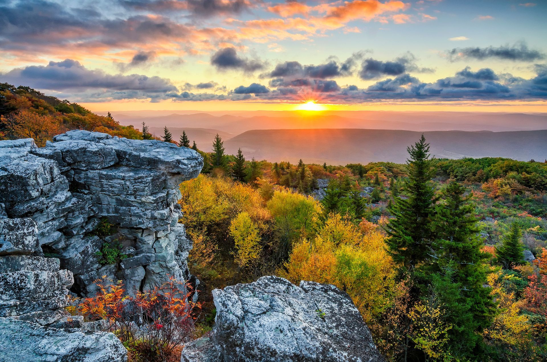 Sunset over mountains with colorful autumn foliage and rocky foreground.