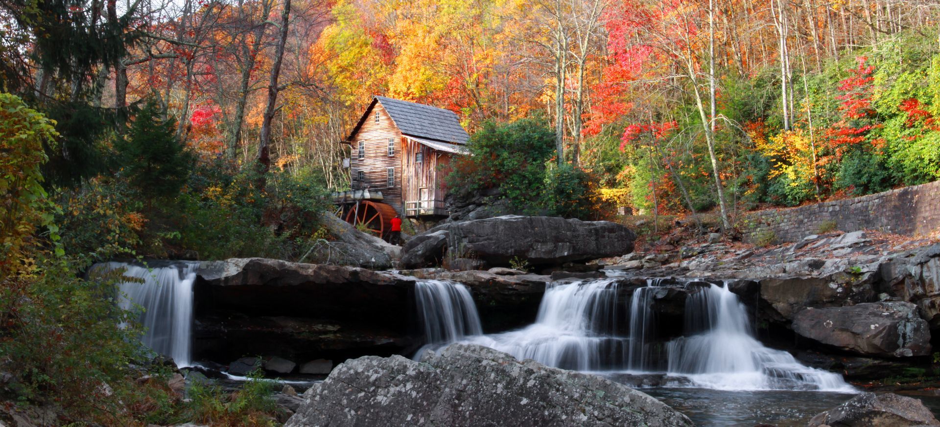 Autumn scene: Waterfall flows past a rustic wooden mill, surrounded by colorful foliage.
