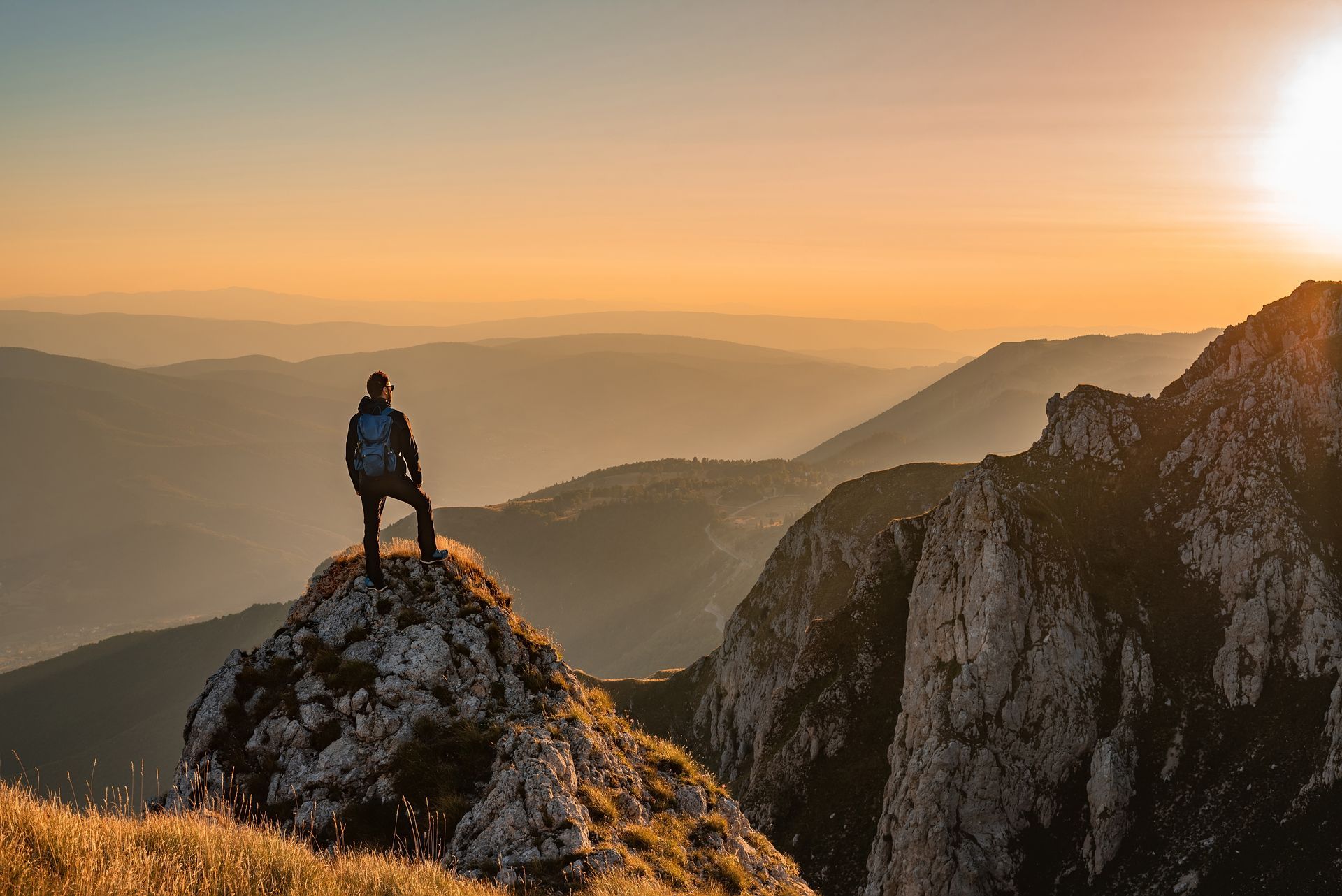 Person on a mountain peak looking at a sunrise over a range of mountains.