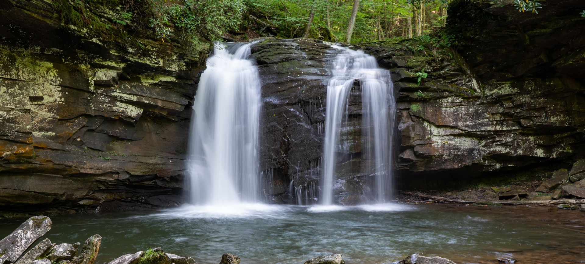 A waterfall cascades into a pool surrounded by rocks and lush green foliage.
