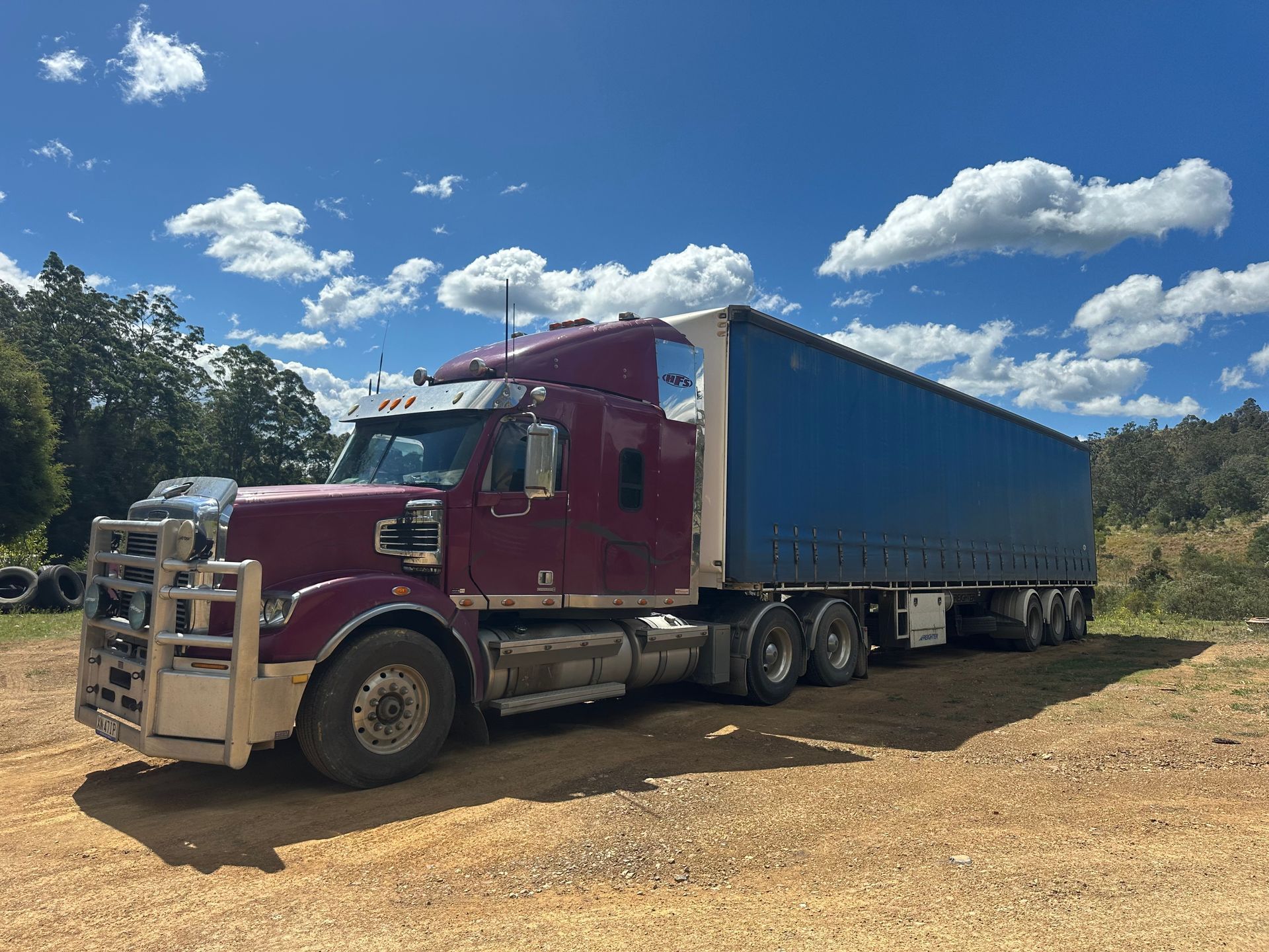 Maroon semi-truck with a blue trailer parked on dirt  — D & M Freighters Water In Bucca Wauka, NSW