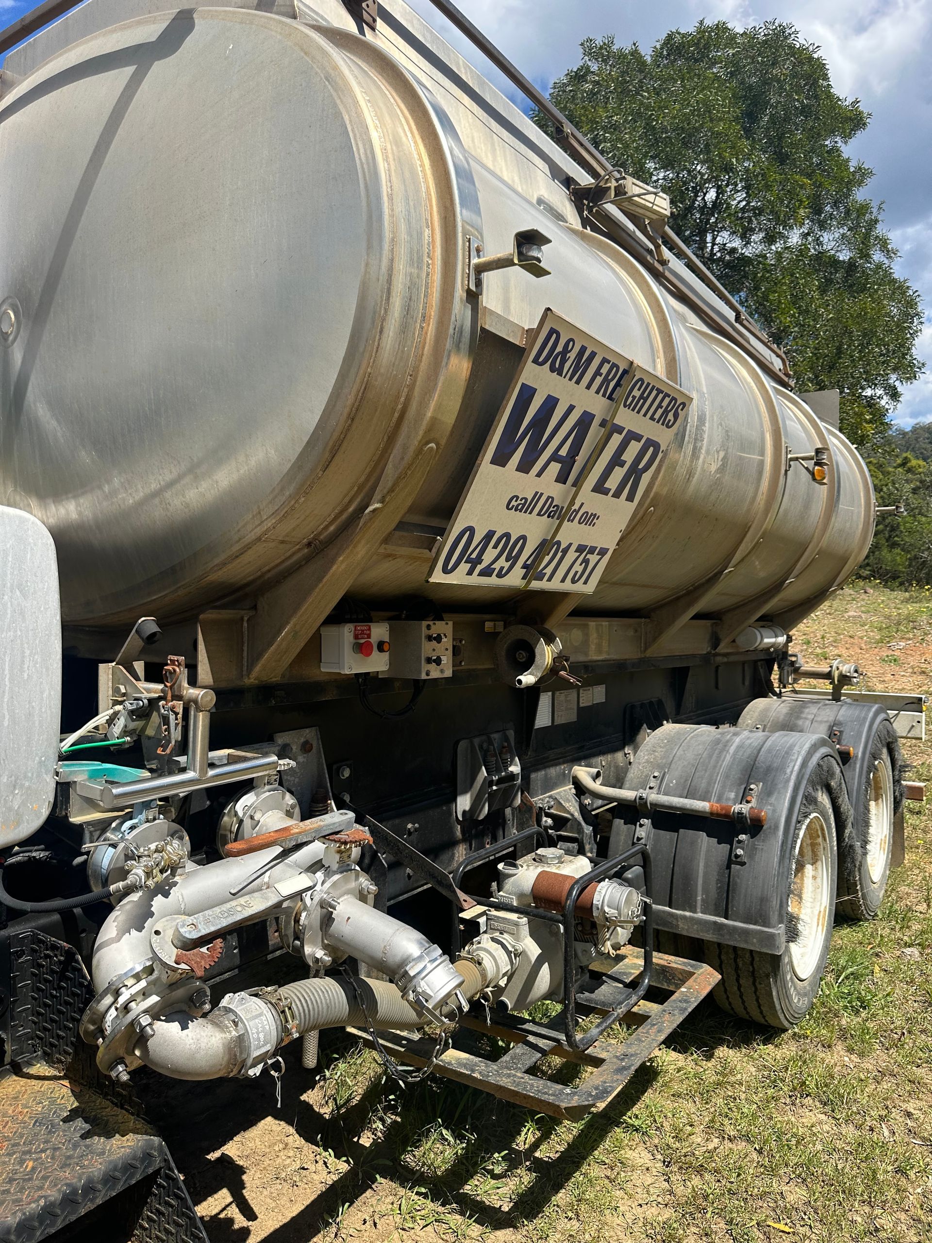 Water tanker truck on grass, displaying a phone number — D & M Freighters Water In Stroud, NSW