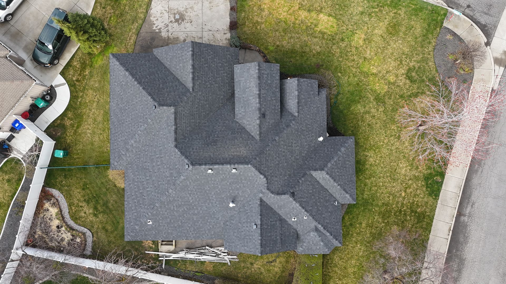 Aerial view of a gray house roof surrounded by a grassy yard and driveway