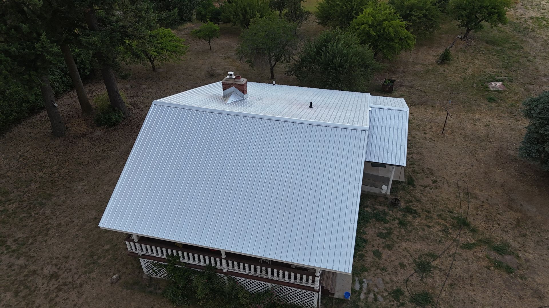 Aerial view of a small white-roofed house surrounded by trees and dirt ground.