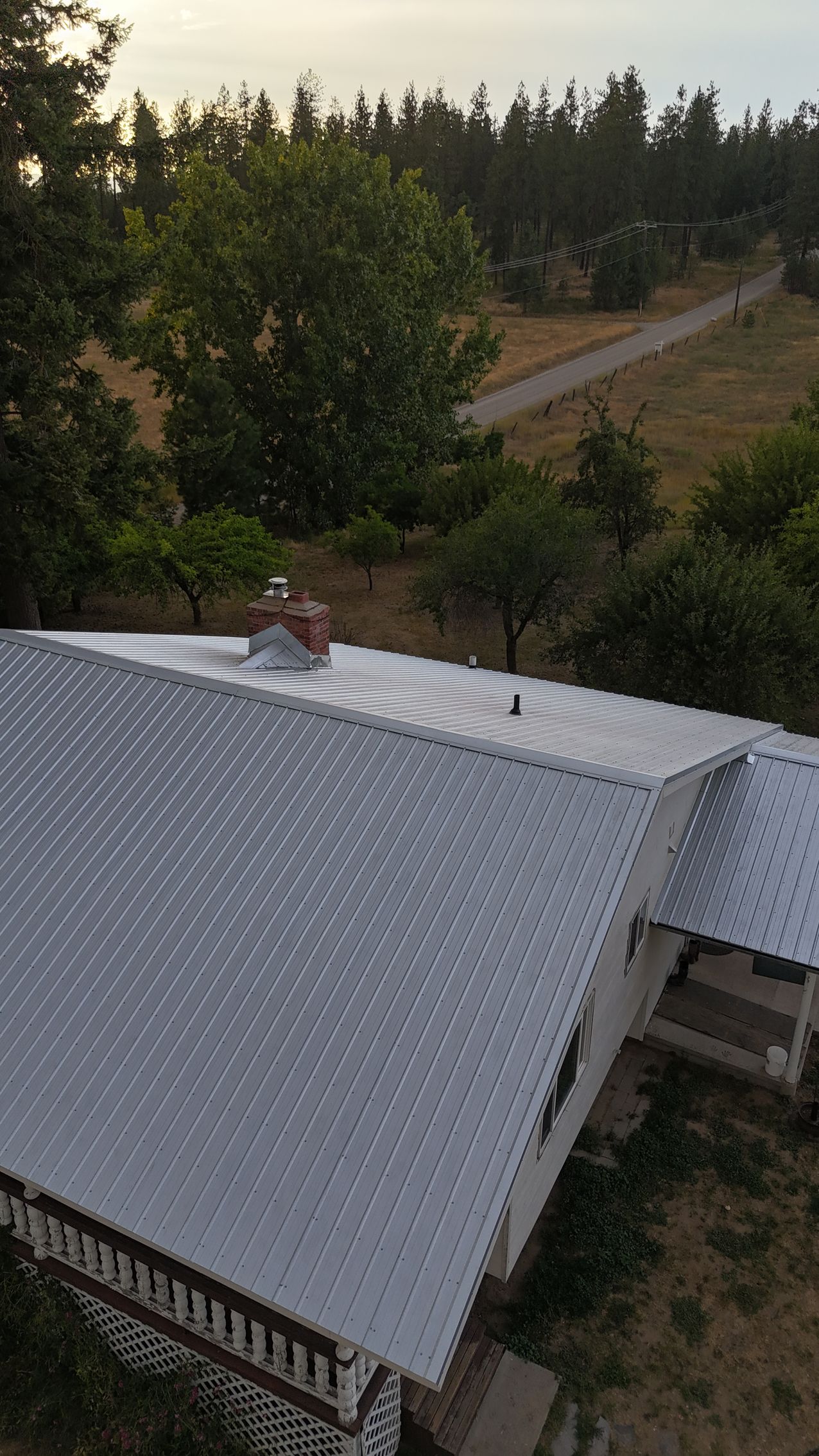 Aerial view of a house with a dark blue metal roof and brick walls in a rural area.