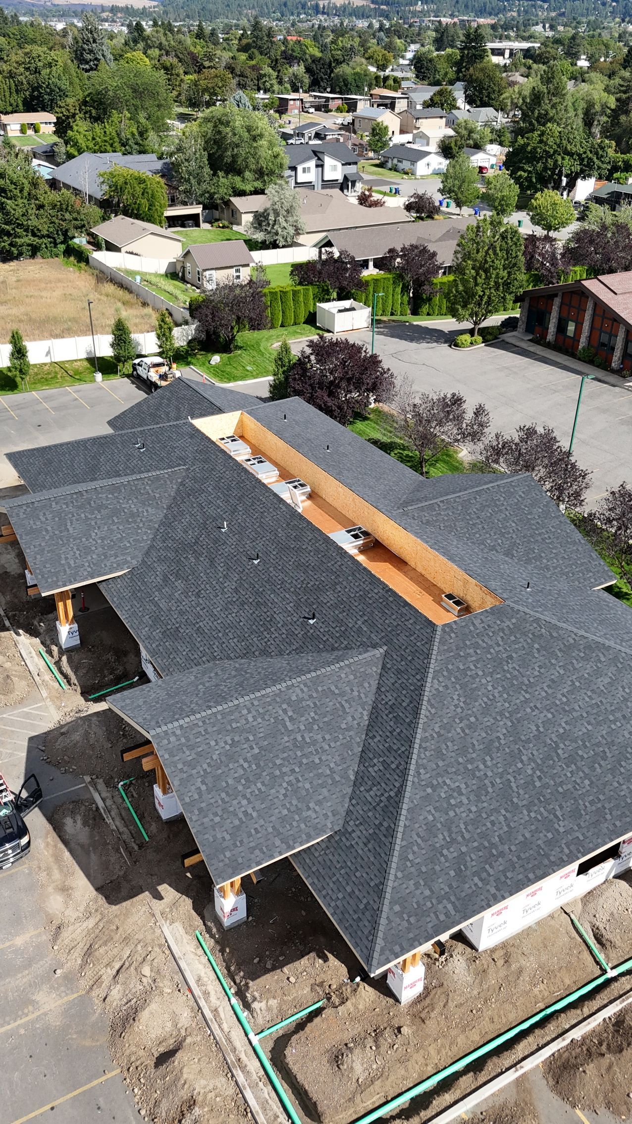 Aerial view of a house with a dark roof in a suburban neighborhood with trees and nearby homes.
