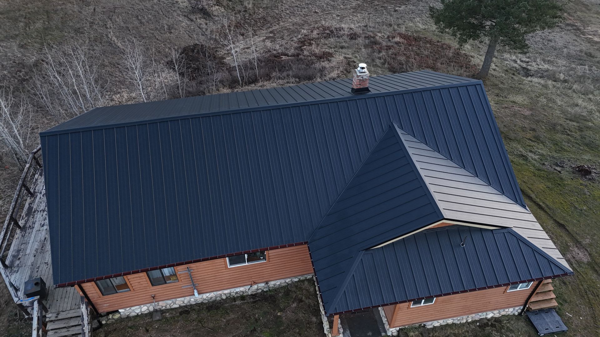Aerial view of a house with a dark blue metal roof and brick walls in a rural area.