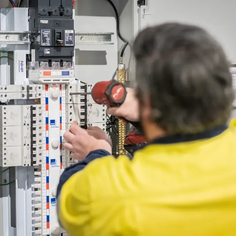 An electrician is working on an electrical box with a drill.